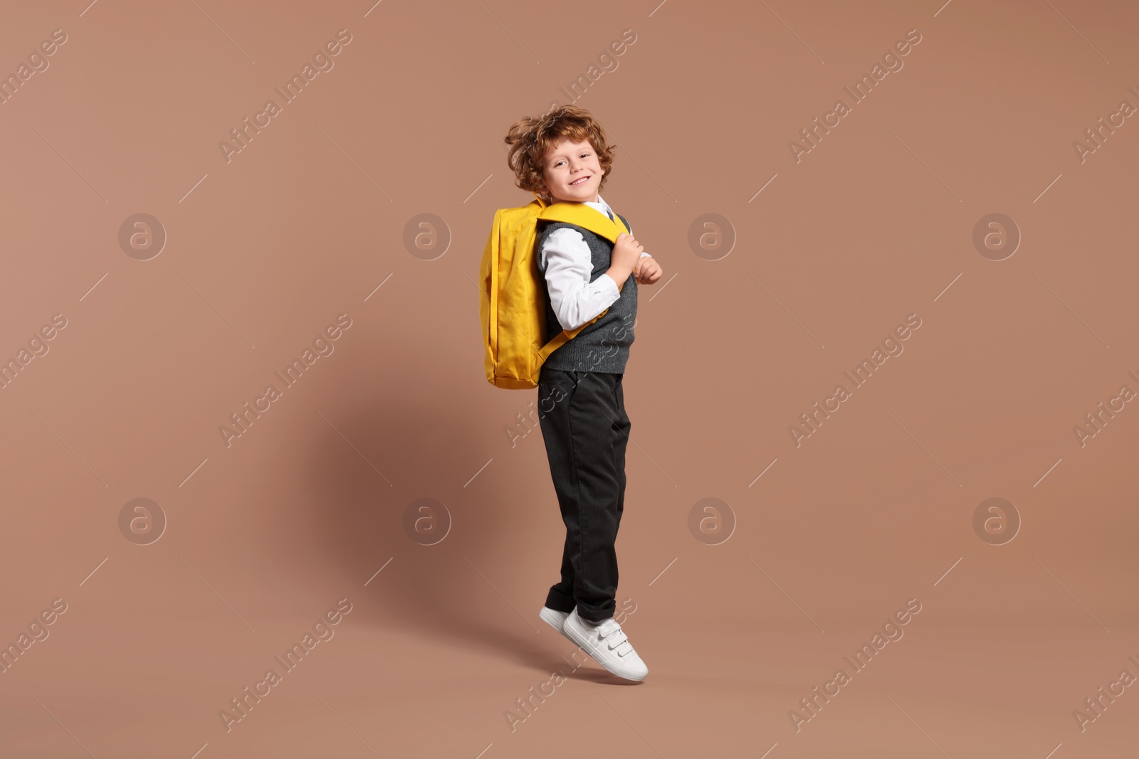 Photo of Happy schoolboy with backpack jumping on brown background