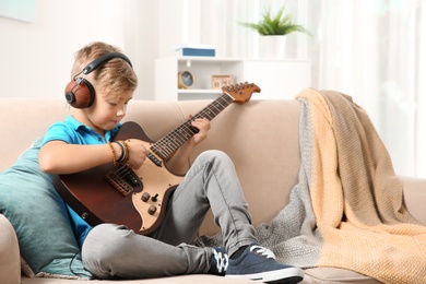 Cute little boy with headphones playing guitar on sofa in room. Space for text
