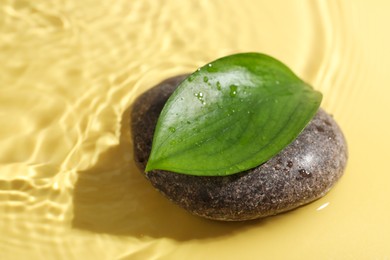 Photo of Spa stone and green leaf on yellow background, closeup