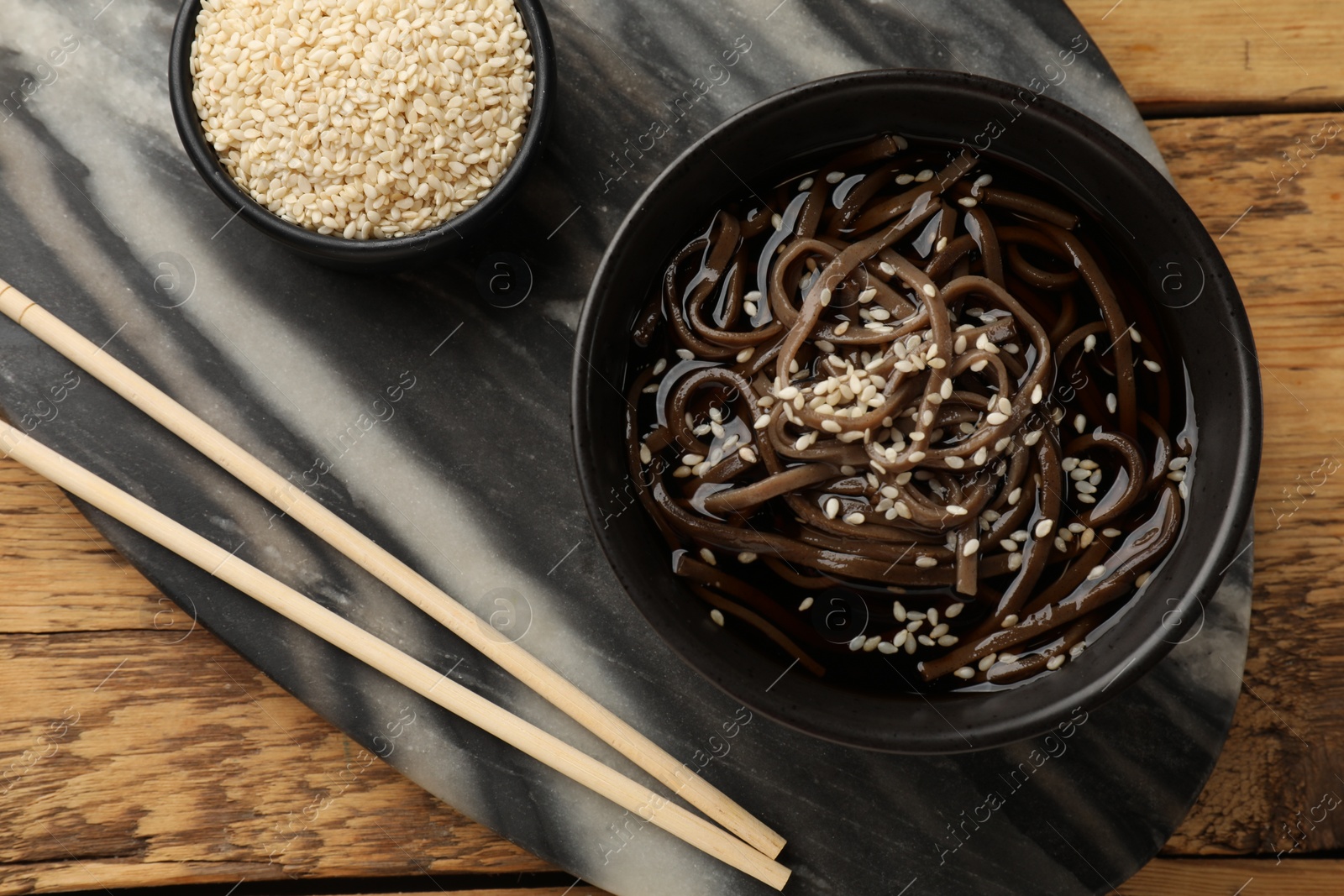 Photo of Tasty soup with buckwheat noodles (soba), sesame and chopsticks on wooden table, flat lay