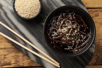 Photo of Tasty soup with buckwheat noodles (soba), sesame and chopsticks on wooden table, flat lay