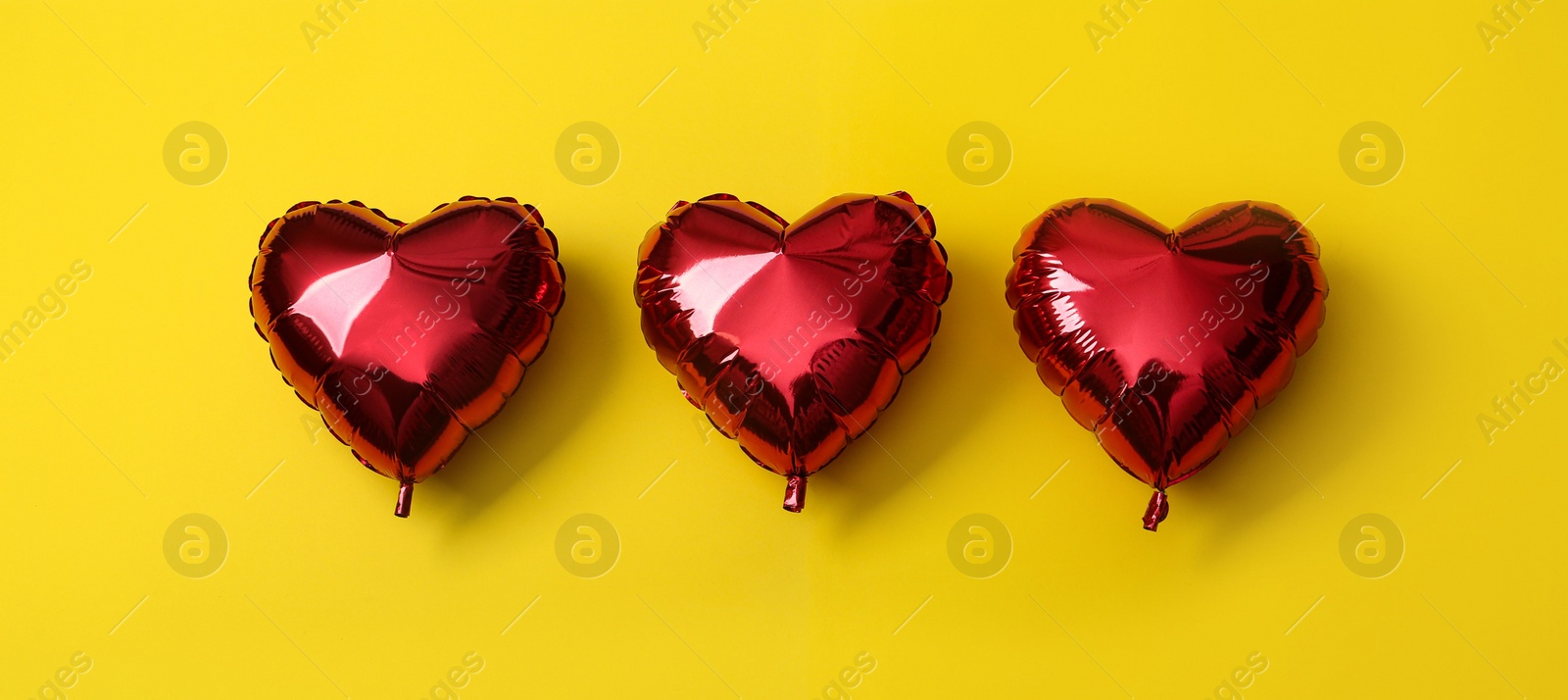 Photo of Red heart shaped balloons on yellow background. Valentine's Day celebration