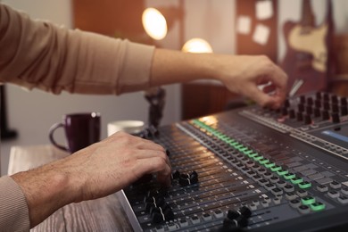 Photo of Man working with professional mixing console in modern radio studio, closeup