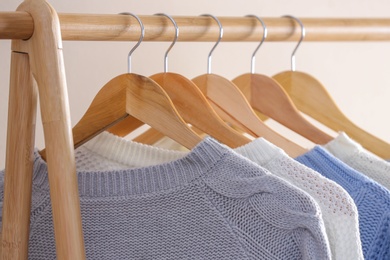 Photo of Collection of warm sweaters hanging on rack near light wall, closeup