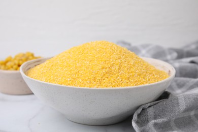 Photo of Raw cornmeal in bowl on white table, closeup