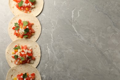 Photo of Delicious tacos with vegetables and parsley on grey marble table, top view. Space for text