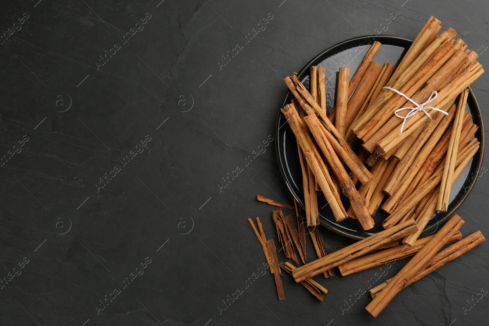 Photo of Aromatic cinnamon sticks on black table, flat lay. Space for text