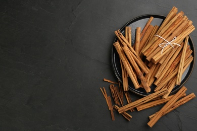 Aromatic cinnamon sticks on black table, flat lay. Space for text