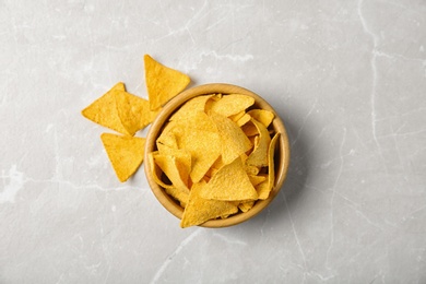 Photo of Tasty mexican nachos chips in wooden bowl on grey table, flat lay