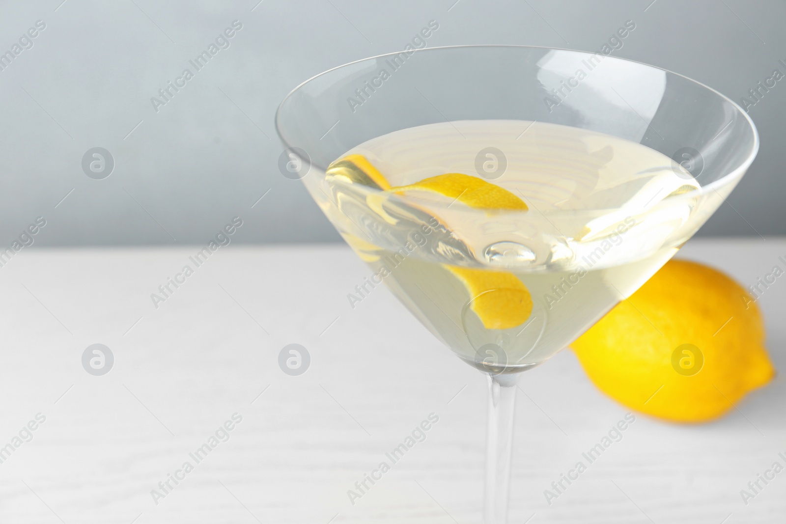 Photo of Glass of lemon drop martini cocktail with zest on white wooden table against grey background, closeup. Space for text