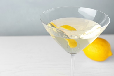 Photo of Glass of lemon drop martini cocktail with zest on white wooden table against grey background, closeup. Space for text