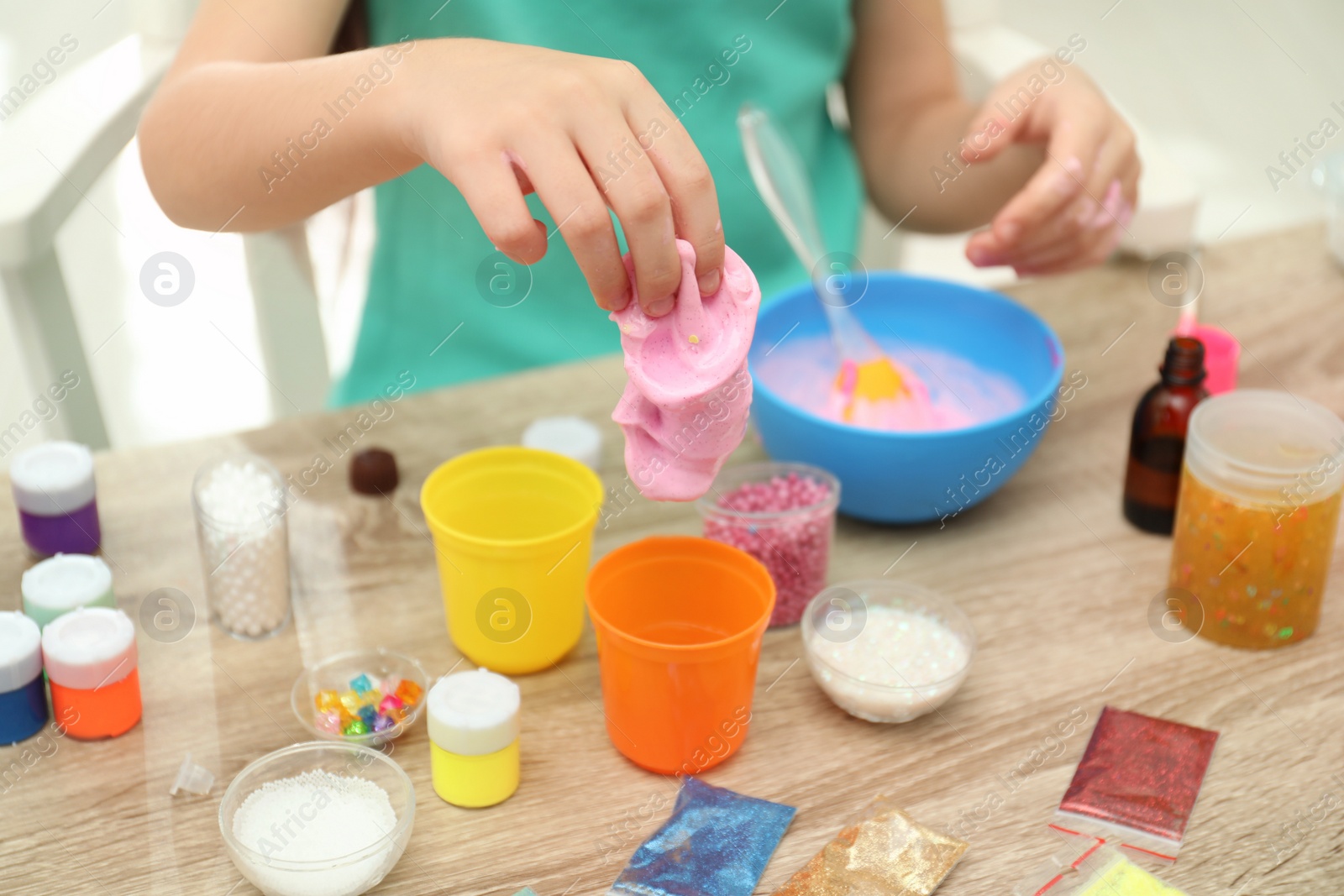 Photo of Little girl making DIY slime toy at table indoors, closeup