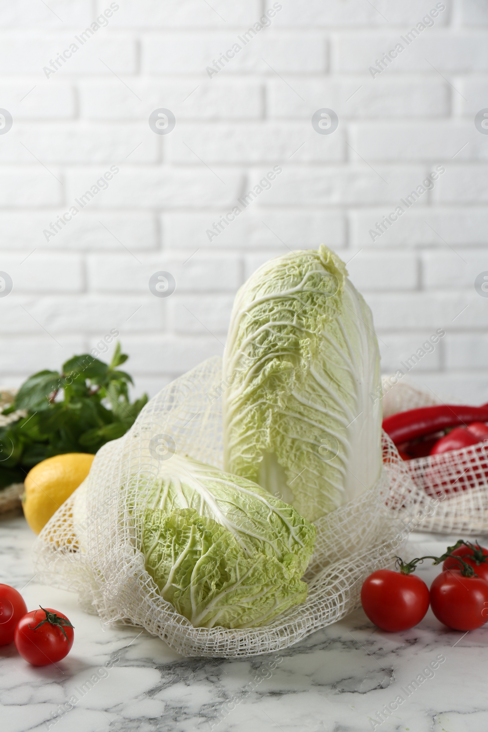 Photo of Fresh Chinese cabbages and other vegetables on white marble table near brick wall