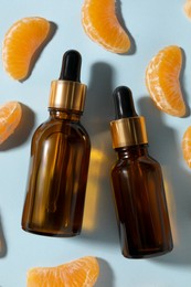 Photo of Aromatic tangerine essential oil in bottles and citrus fruits on light blue table, flat lay