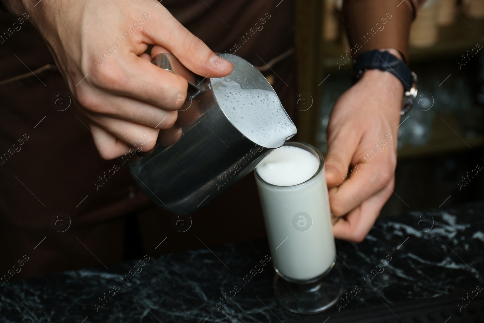 Photo of Barista pouring milk into glass cup for coffee drink at table