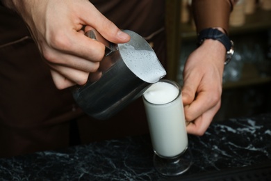 Photo of Barista pouring milk into glass cup for coffee drink at table