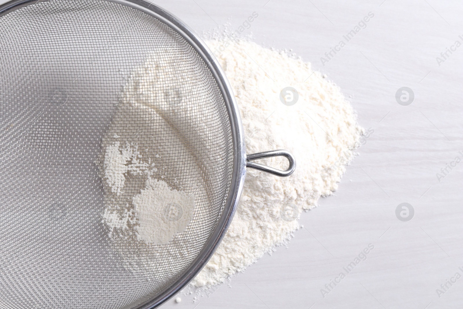 Photo of Metal sieve and flour on white wooden table, top view. Space for text