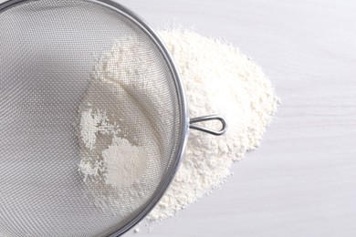 Photo of Metal sieve and flour on white wooden table, top view. Space for text