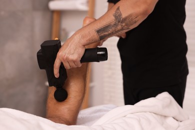 Photo of Man receiving professional leg massage with electric gun in spa salon, closeup