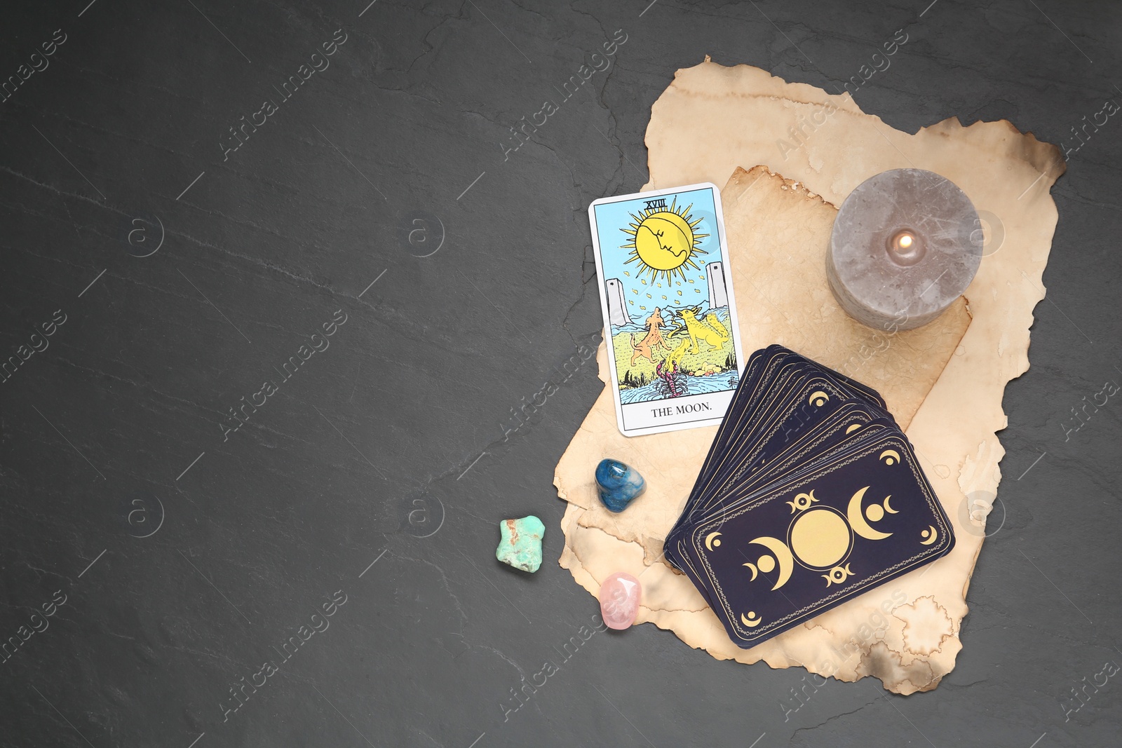 Photo of The Moon with other tarot cards, candle and gemstones on black table, flat lay. Space for text