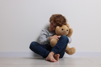 Photo of Child abuse. Upset boy with toy sitting on floor near white wall