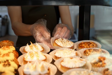 Photo of Seller taking tasty tartlet from showcase in bakery shop, closeup