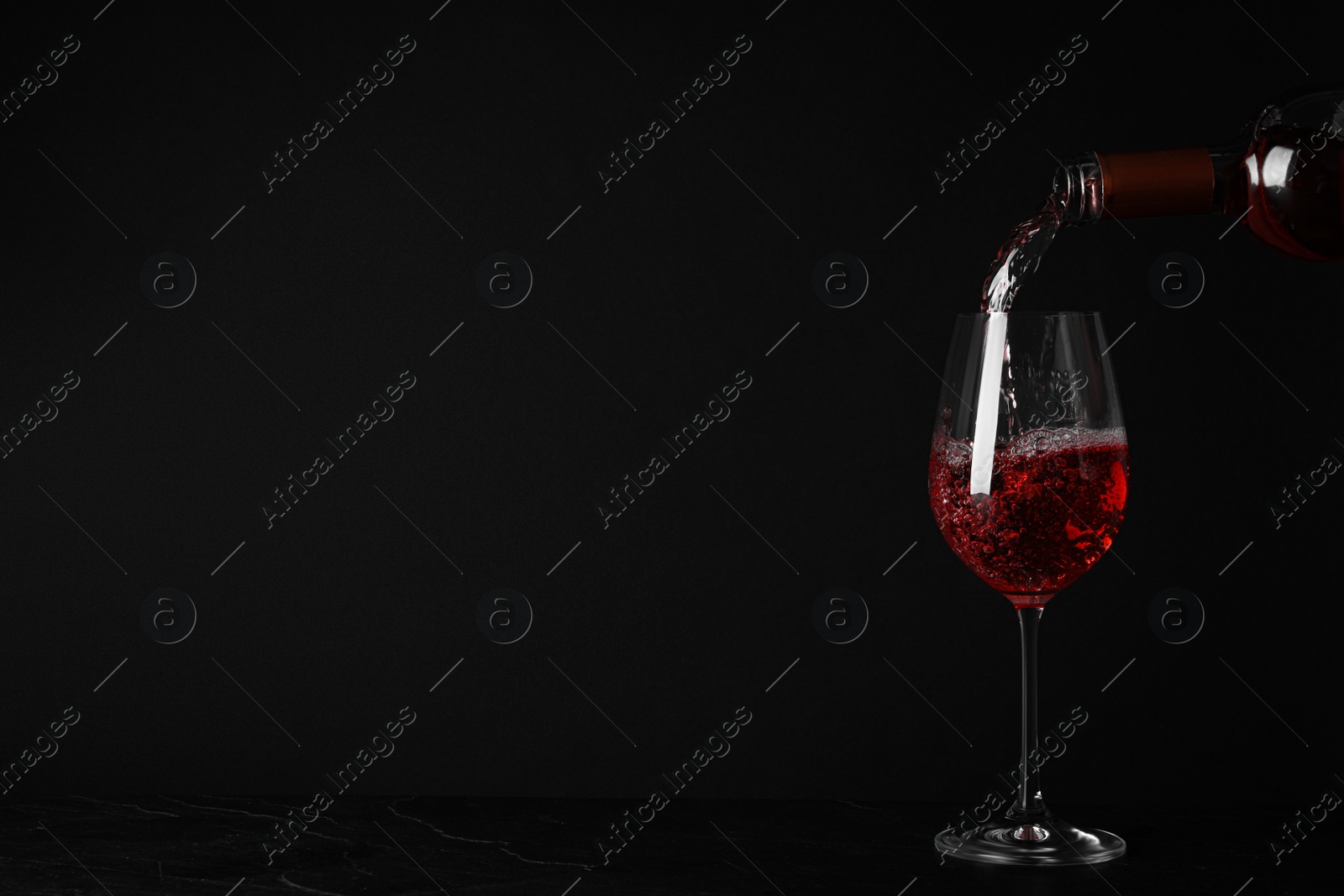 Photo of Pouring delicious rose wine into glass on table against black background. Space for text