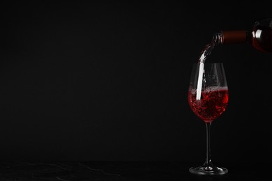 Pouring delicious rose wine into glass on table against black background. Space for text
