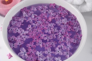 Photo of Bowl of aromatic water with lilac flowers on white table, closeup