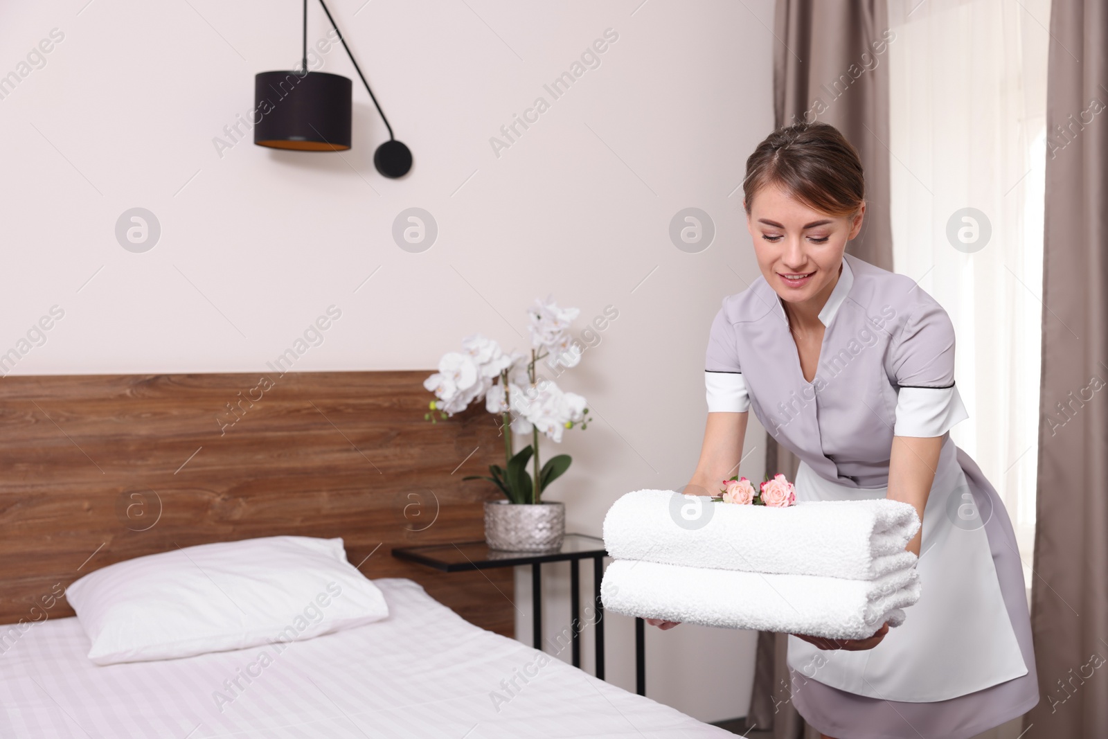 Photo of Beautiful chambermaid putting fresh towels on bed in hotel room