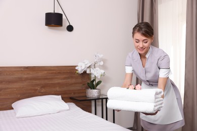 Beautiful chambermaid putting fresh towels on bed in hotel room