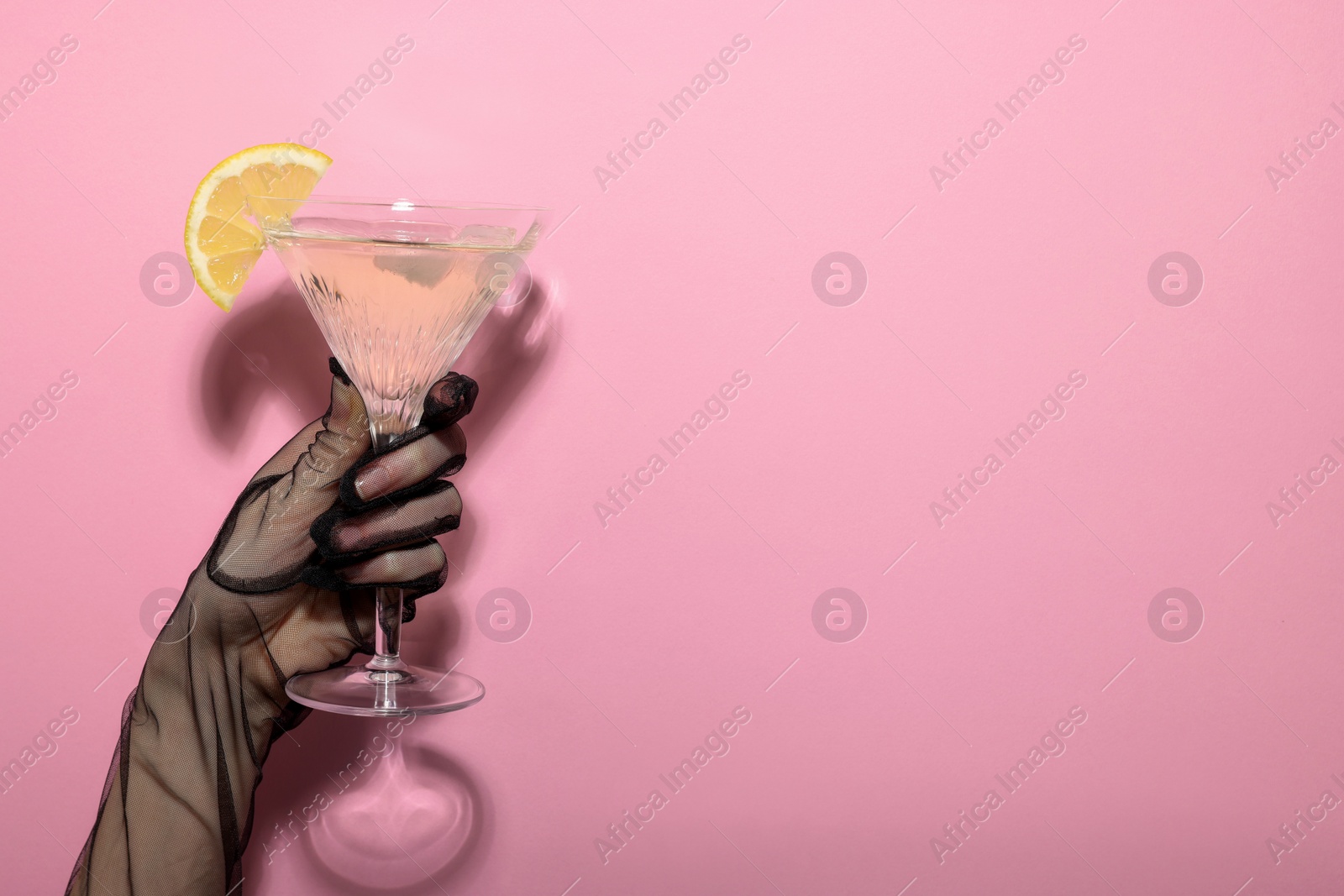 Photo of Woman holding martini glass of refreshing cocktail with lemon slice on pink background, closeup. Space for text
