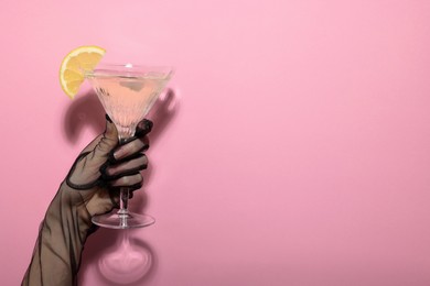 Photo of Woman holding martini glass of refreshing cocktail with lemon slice on pink background, closeup. Space for text