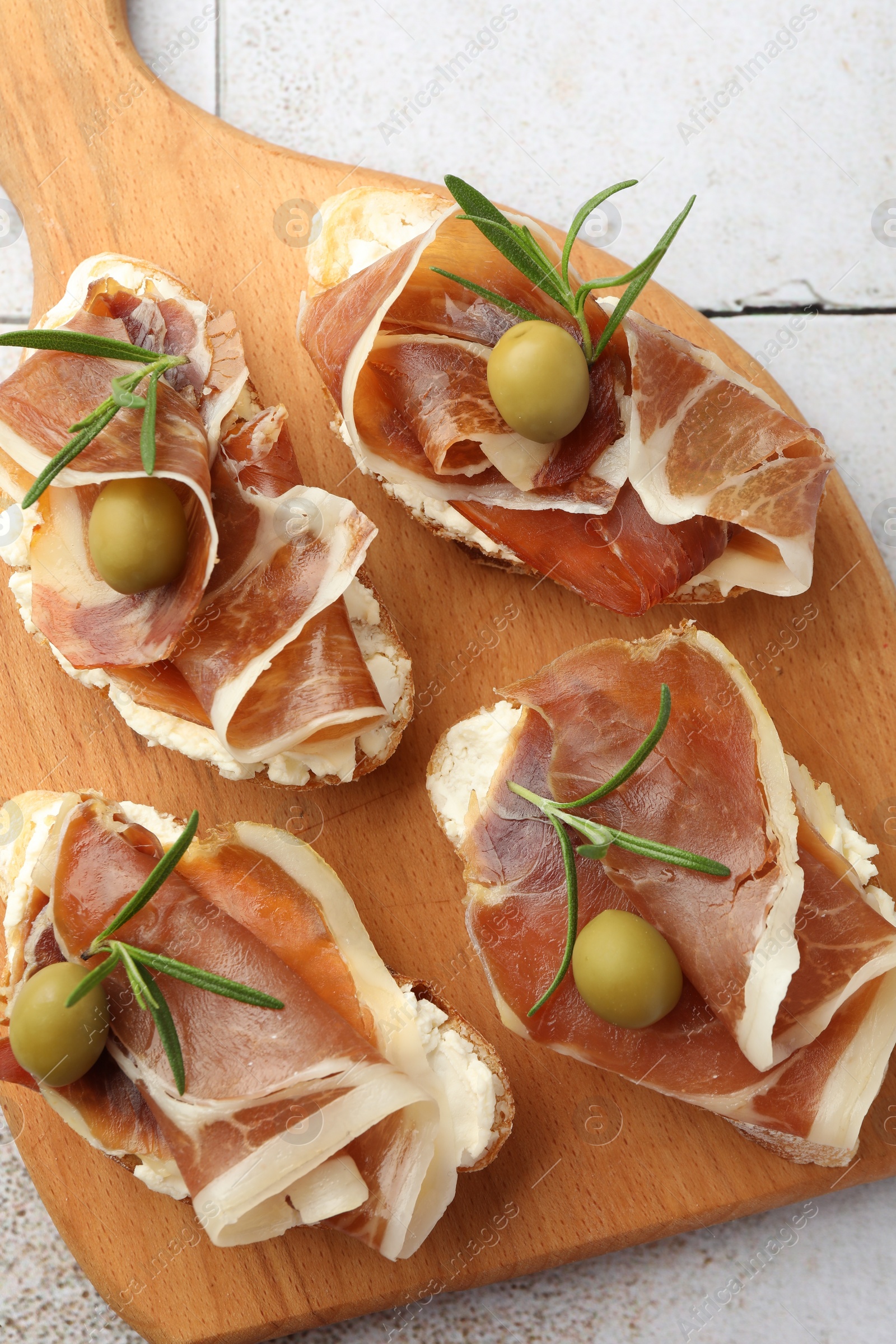 Photo of Tasty sandwiches with cured ham, rosemary and olives on tiled table, top view