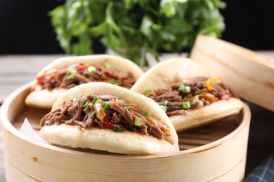 Photo of Delicious gua bao in bamboo steamer on wooden table, closeup