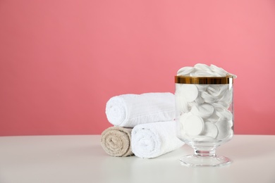 Jar with cotton pads on white table against pink background. Space for text