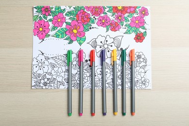 Photo of Antistress coloring page and felt tip pens on light wooden table, flat lay