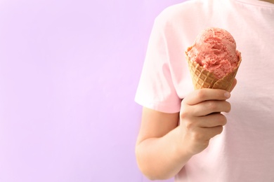 Woman holding ice cream in wafer cone on pink background, closeup. Space for text