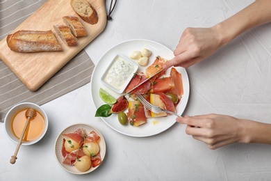 Photo of Woman cutting melon and prosciutto appetizer on table, top view