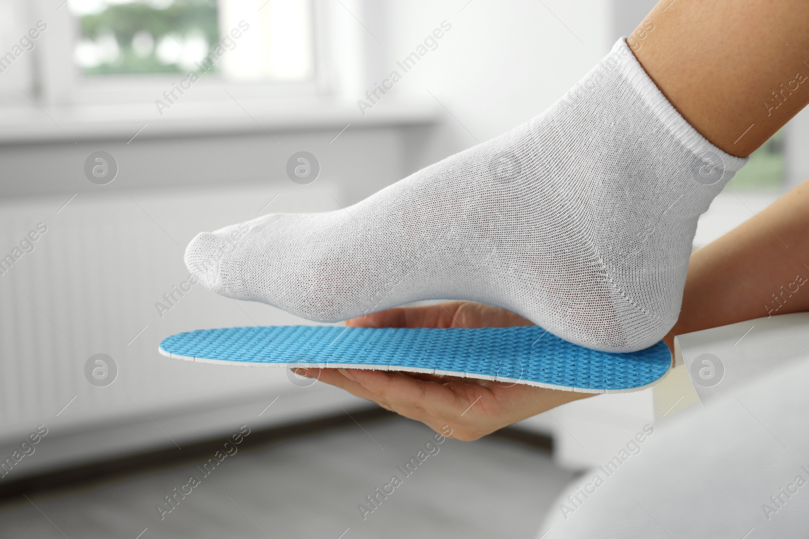 Photo of Woman fitting orthopedic insole to her foot indoors, closeup