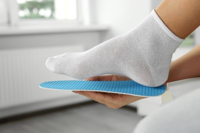 Woman fitting orthopedic insole to her foot indoors, closeup