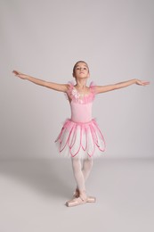 Photo of Beautifully dressed little ballerina dancing on grey background