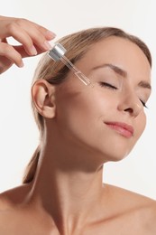 Photo of Beautiful woman applying cosmetic serum onto her face on white background