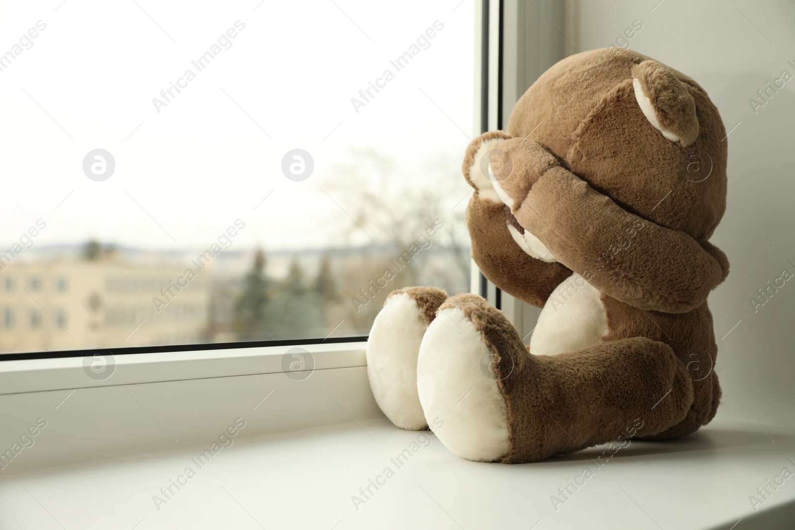 Photo of Cute lonely teddy bear on windowsill indoors. Space for text