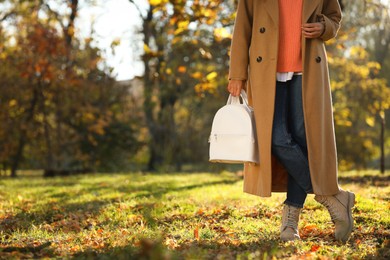 Photo of Young woman with stylish white backpack in autumn park, closeup. Space for text