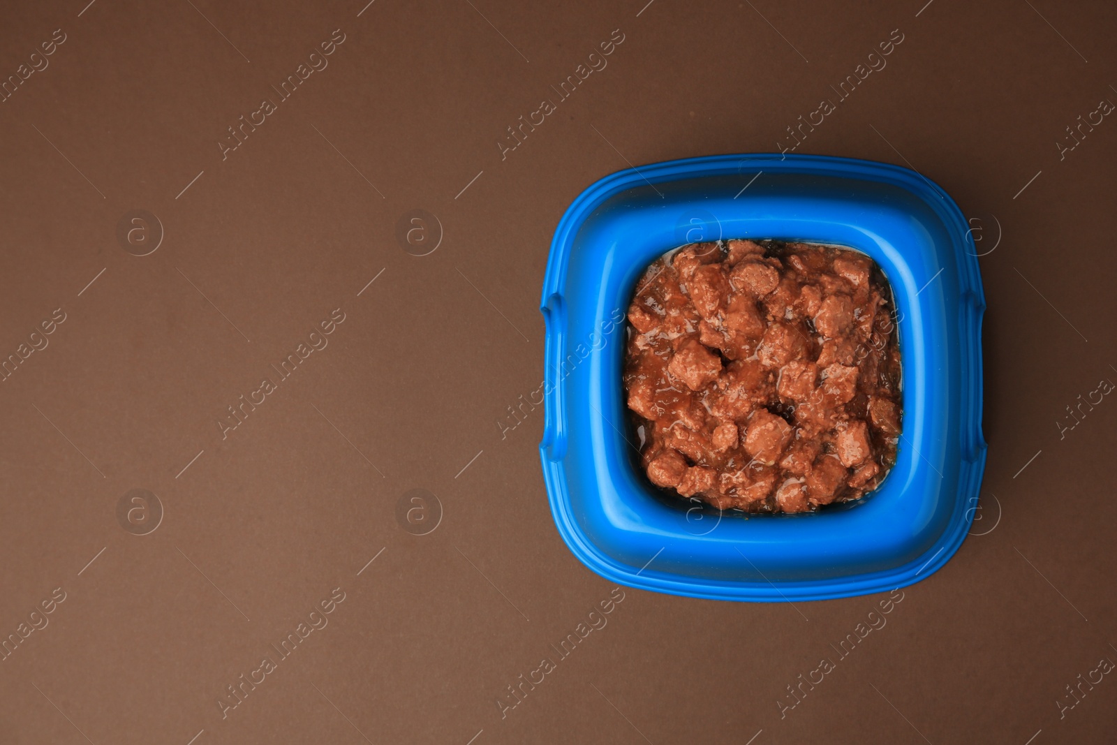 Photo of Wet pet food in feeding bowl on brown background, top view. Space for text