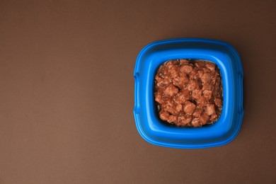 Photo of Wet pet food in feeding bowl on brown background, top view. Space for text