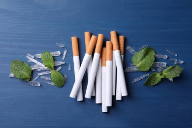 Photo of Cigarettes, menthol crystals and mint leaves on blue wooden table, flat lay