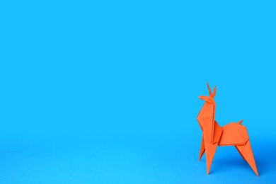 Photo of Origami art. Handmade orange paper deer on light blue background, space for text