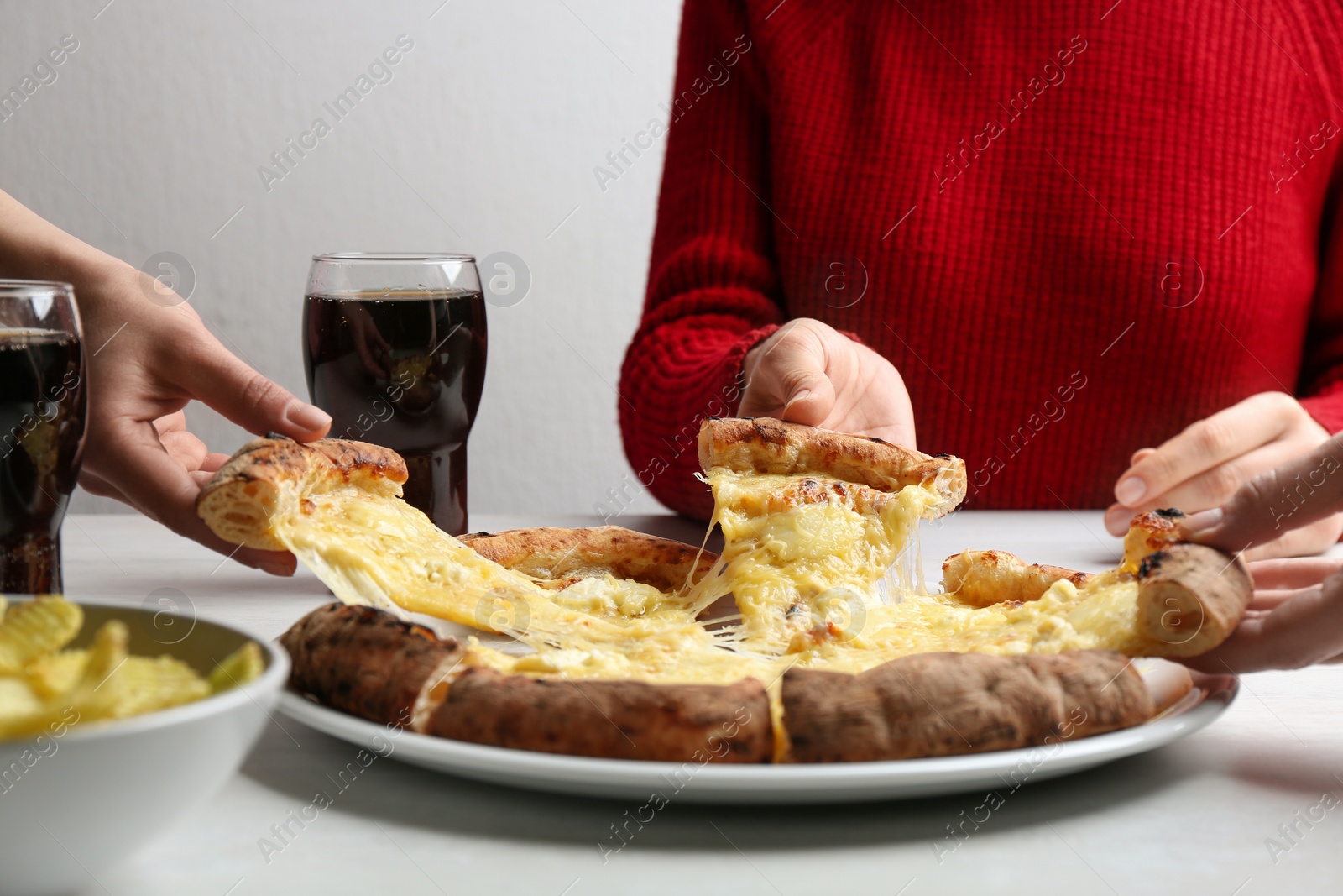 Photo of People taking pieces of delicious cheese pizza at white table, closeup